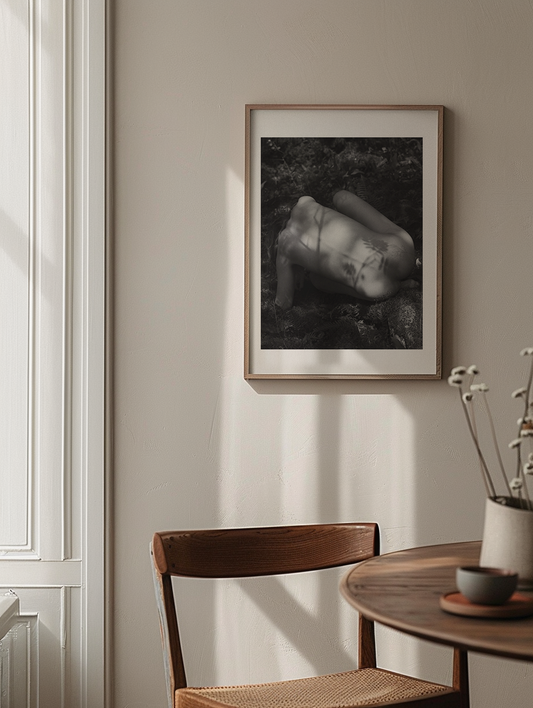 Framed black and white artwork on a wall above a wooden chair and table.