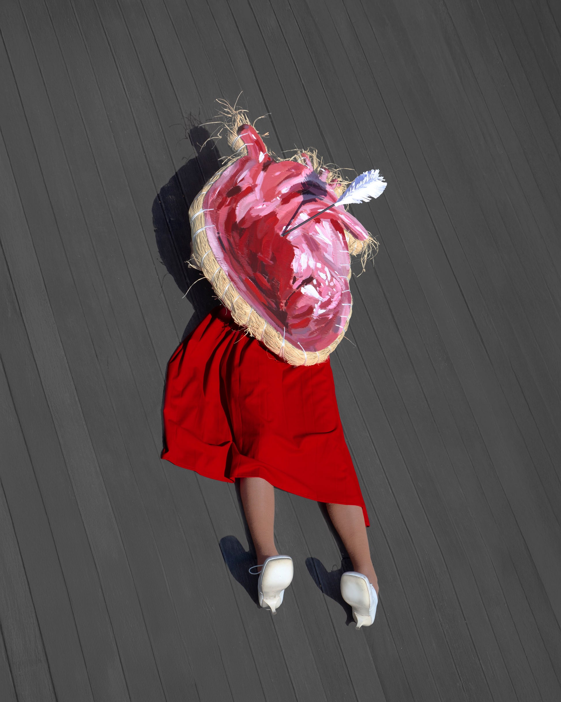 Person wearing a red dress with a heart-shaped head on a dark wooden floor.