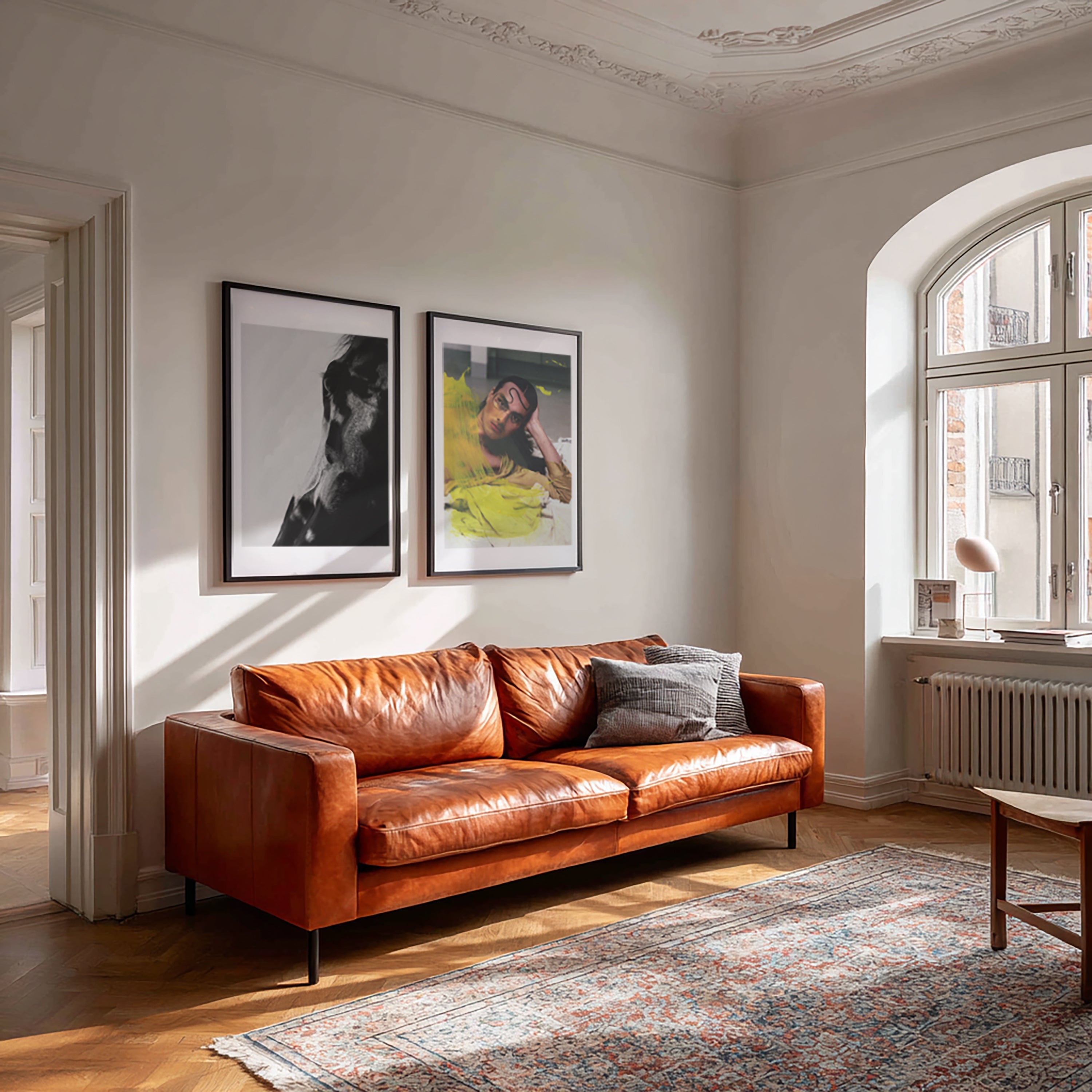 Living room with a brown leather sofa, framed pictures on the wall, and a large window.