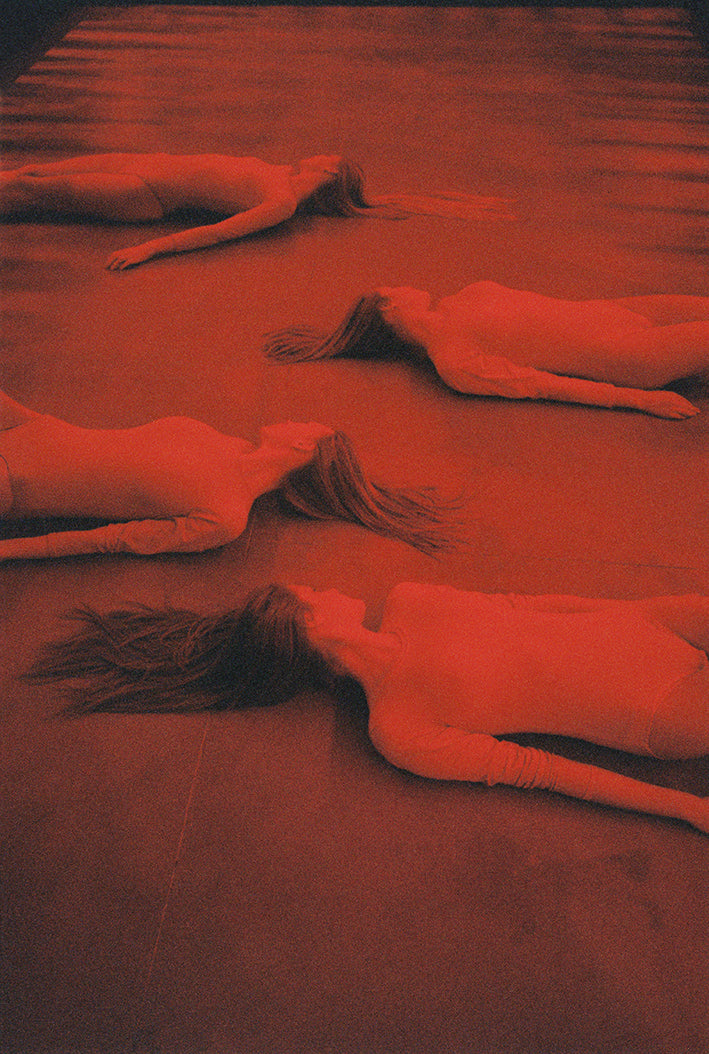 A poster featuring a surrealistic image with multiple figures lying on a red surface.